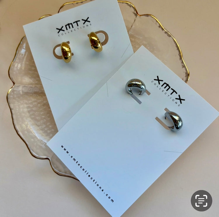 Gold and silver earrings on XMTX Collection cards with a beige background