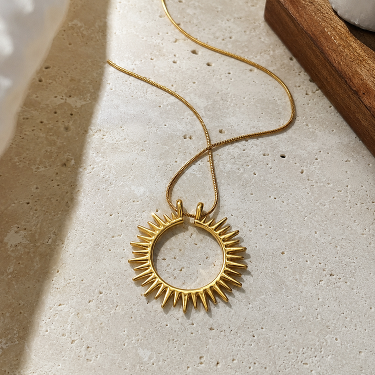 Flat lay of the Sunray Necklace featuring a waterproof non-tarnish gold sun pendant on a neutral stone surface.