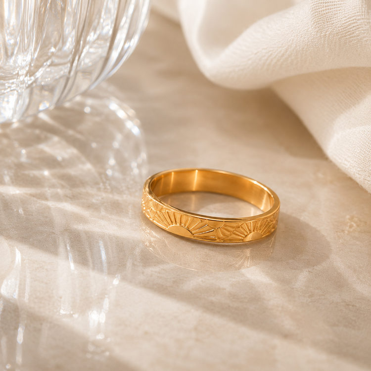 Sun Ring engraved gold band displayed in a luxury editorial flat lay with natural light