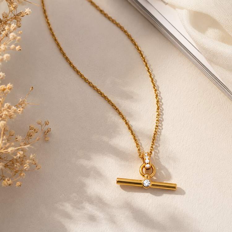 Flat lay of a waterproof gold T Bar pendant necklace with crystal accent on a neutral background, showcasing everyday luxury jewelry