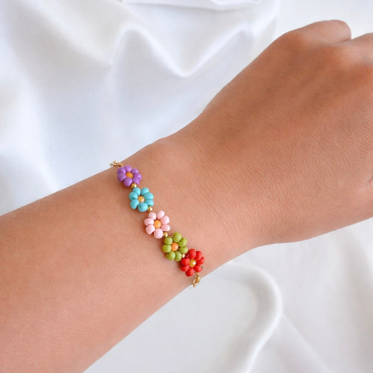Woman wearing the 5 Beaded Daisies Bracelet featuring colorful purple, blue, pink, green, and coral flower beads on a gold chain.