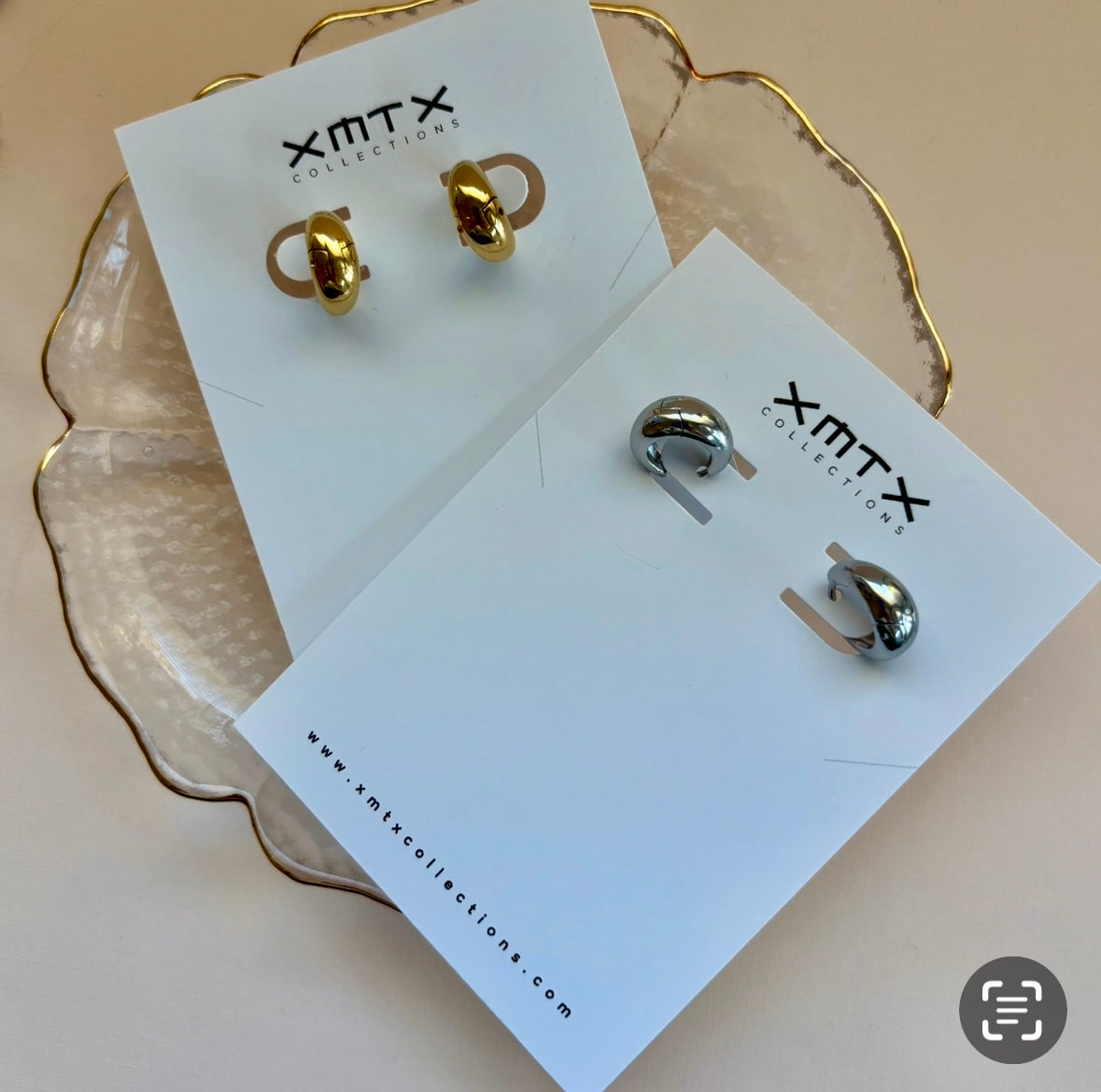 Gold and silver earrings on XMTX Collection cards with a beige background