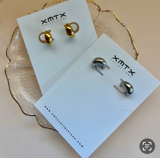 Gold and silver earrings on XMTX Collection cards with a beige background