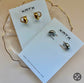 Gold and silver earrings on XMTX Collection cards with a beige background