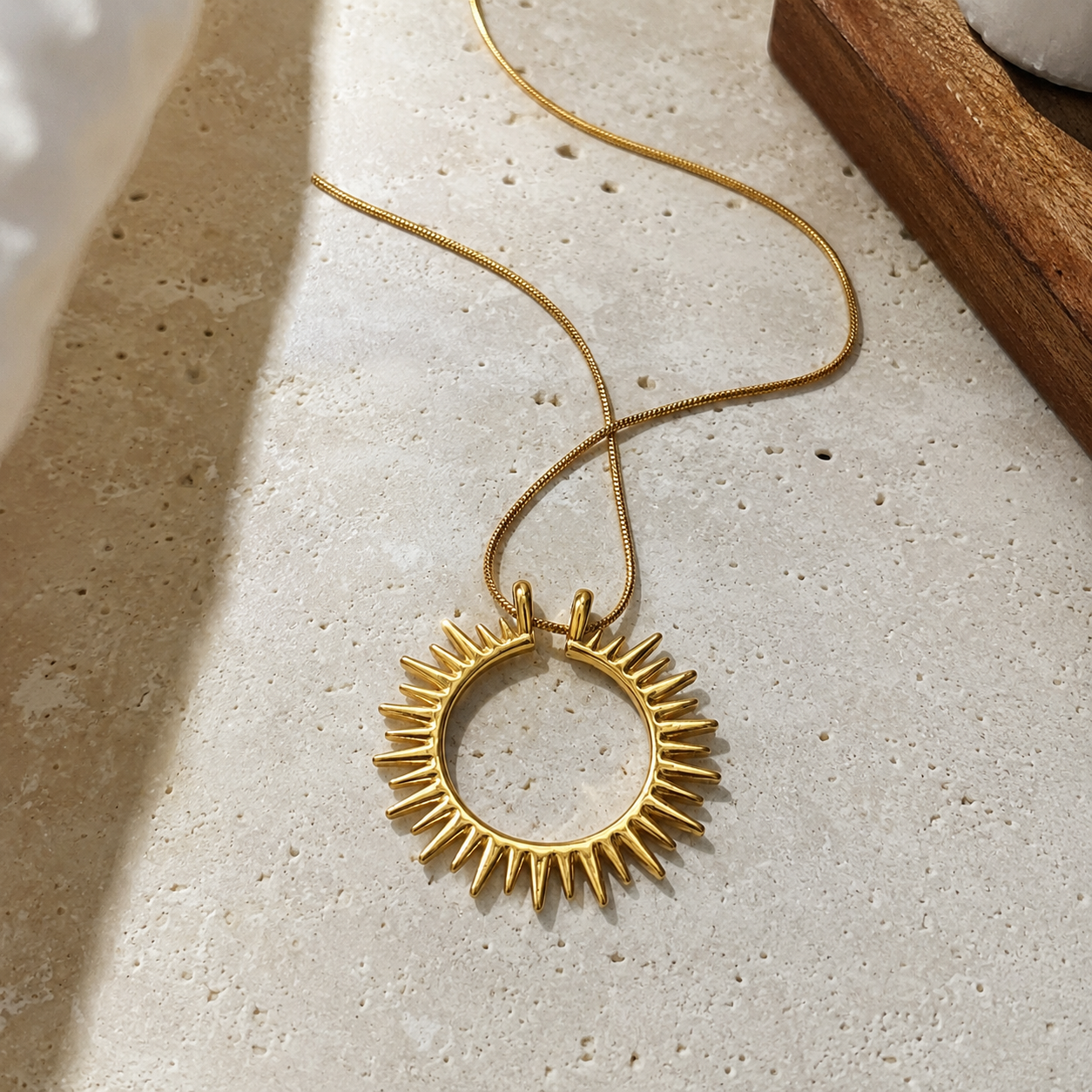 Flat lay of the Sunray Necklace featuring a waterproof non-tarnish gold sun pendant on a neutral stone surface.