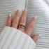 Close-up of Alissa gold ring with green and pink stones held in hand over open book