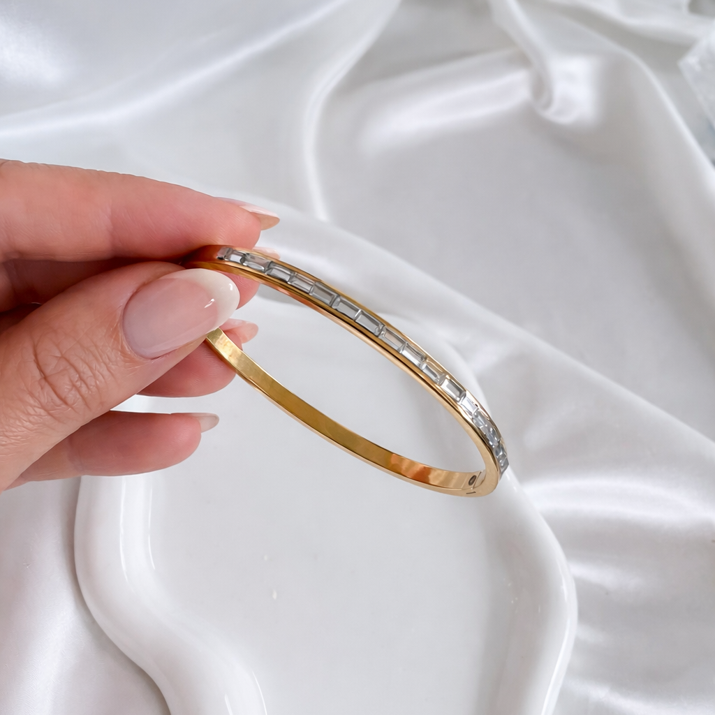 Close-up of the gold Ally bangle bracelet with baguette-cut stones being held by hand