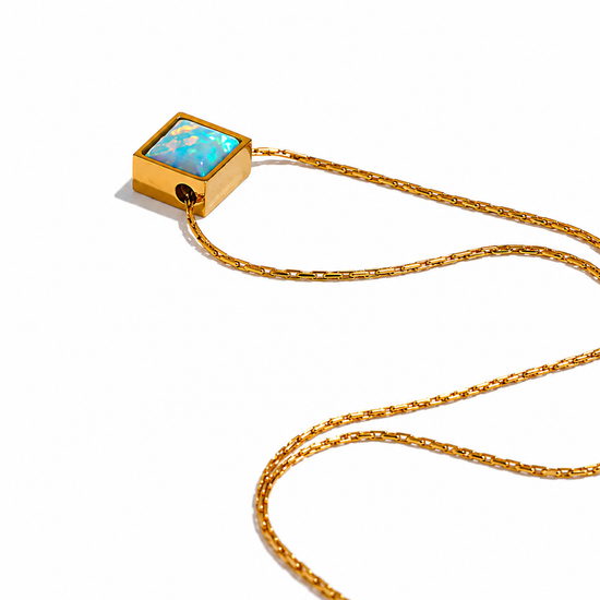 A gold chain necklace featuring a square pendant with a light blue opal inlay set in a gold frame, photographed on a clean white background.