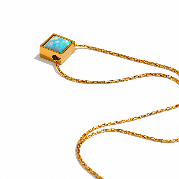 A gold chain necklace featuring a square pendant with a light blue opal inlay set in a gold frame, photographed on a clean white background.