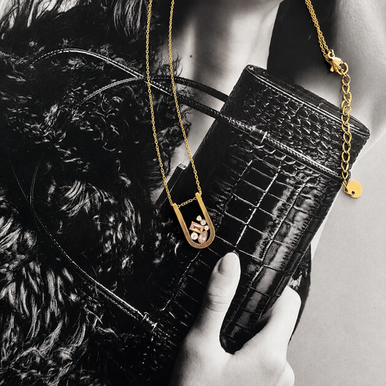 Modern gold Bianka necklace with sparkling multi-cut cubic zirconia pendant styled on a fashion editorial background.