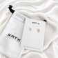 Brenda clear stud earrings displayed on an XMTX Collections jewelry card with branded pouch
