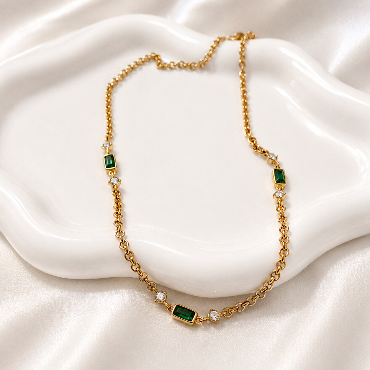 Brielle gold necklace with emerald-green baguette stones styled on a white ceramic jewelry dish