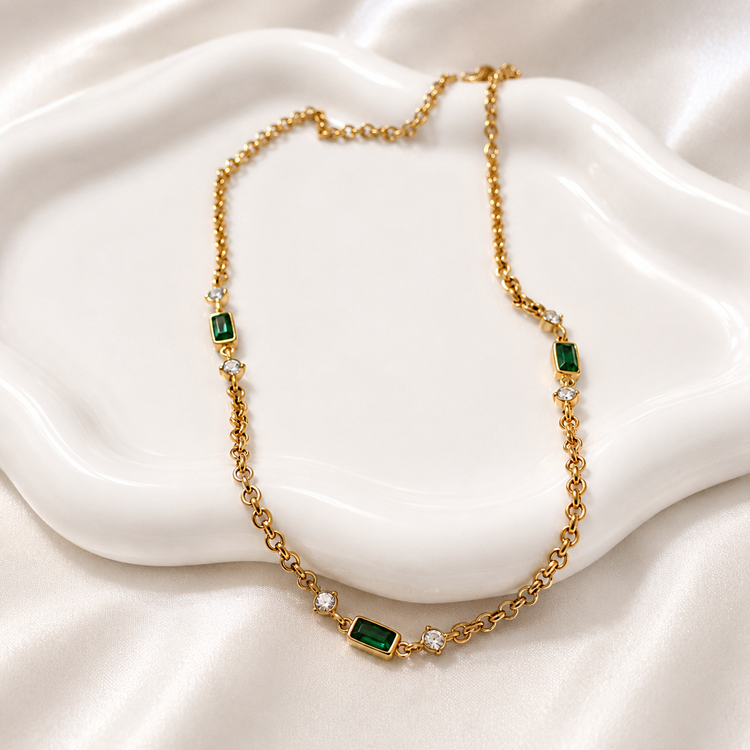 Brielle gold necklace with emerald-green baguette stones styled on a white ceramic jewelry dish