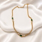 Brielle gold necklace with emerald-green baguette stones styled on a white ceramic jewelry dish