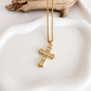 Gold cross necklace with clear stone accents displayed on a white jewelry dish