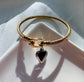 Gold bracelet with a heart-shaped black pendant on a white surface