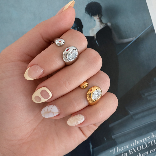 Jennie Ring in gold and silver worn on hand with neutral nail art, featuring a sculptural statement design and round crystal stone.