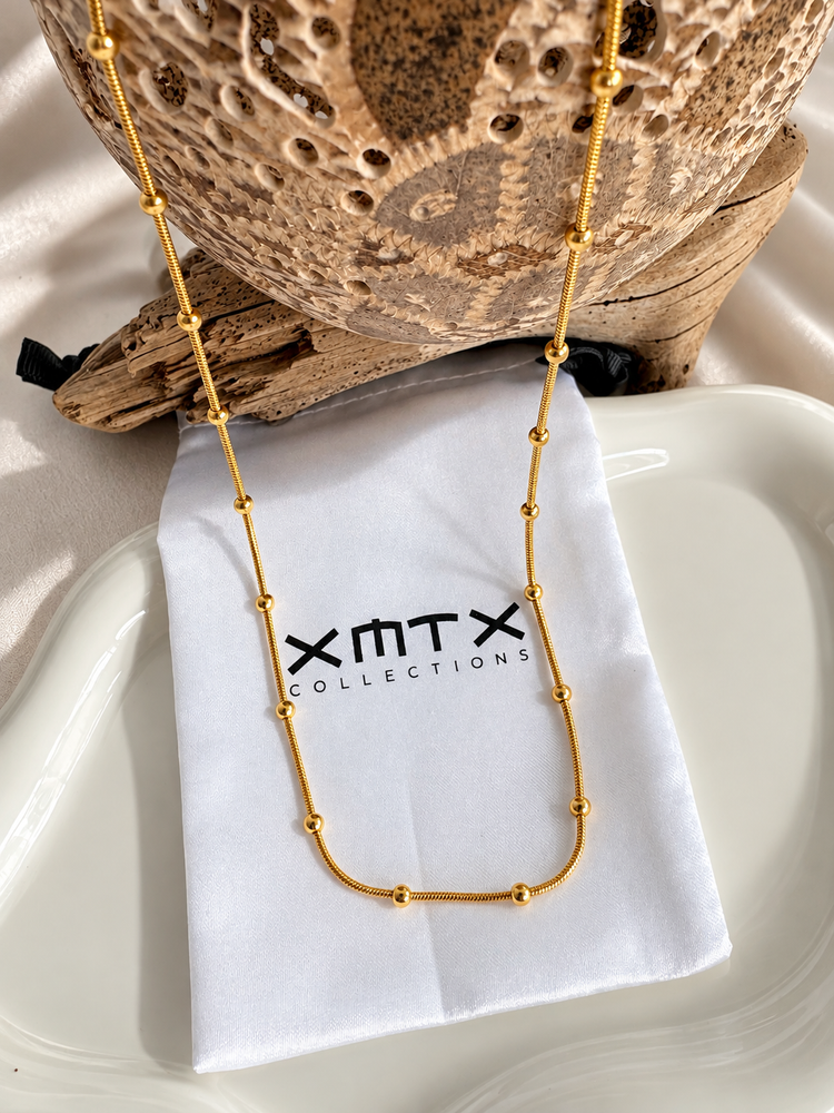 Lyssa Bead Chain Necklace styled on an XMTX Collections jewelry pouch, featuring a delicate gold bead chain