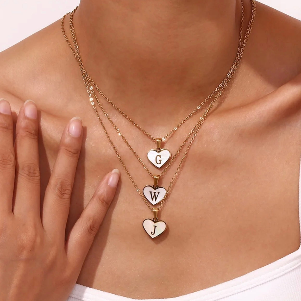 Mother of Pearl Heart Initial Necklace Model wearing a personalized Mother of Pearl heart initial necklace layered with other gold necklaces. Waterproof, non-tarnish everyday jewelry by XMTX Collections