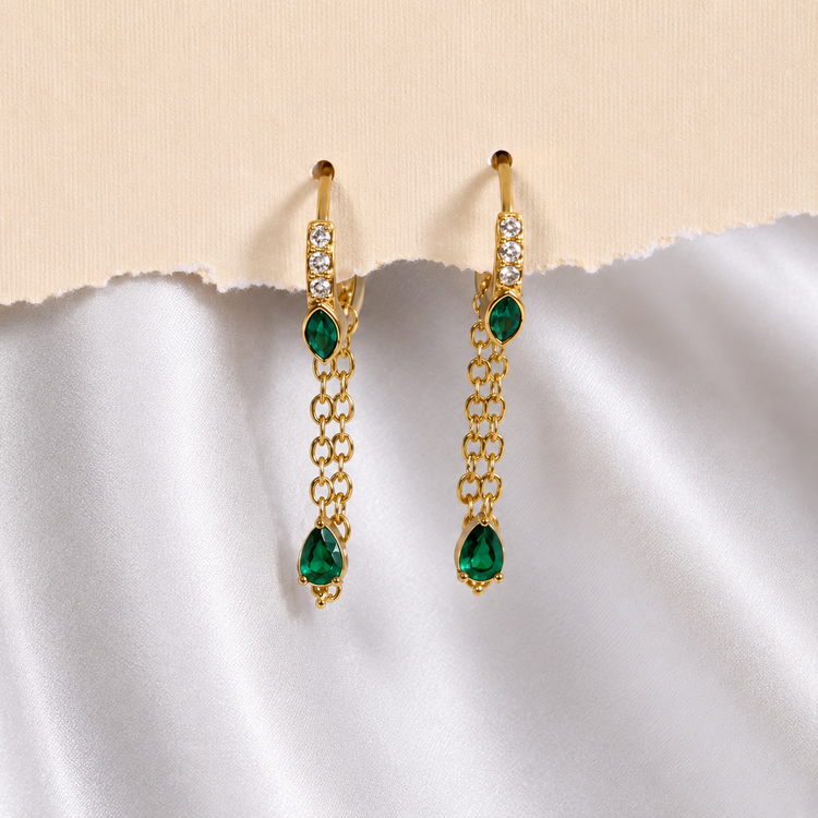 Pair of Sallie waterproof gold tassel huggie earrings displayed on soft white fabric
