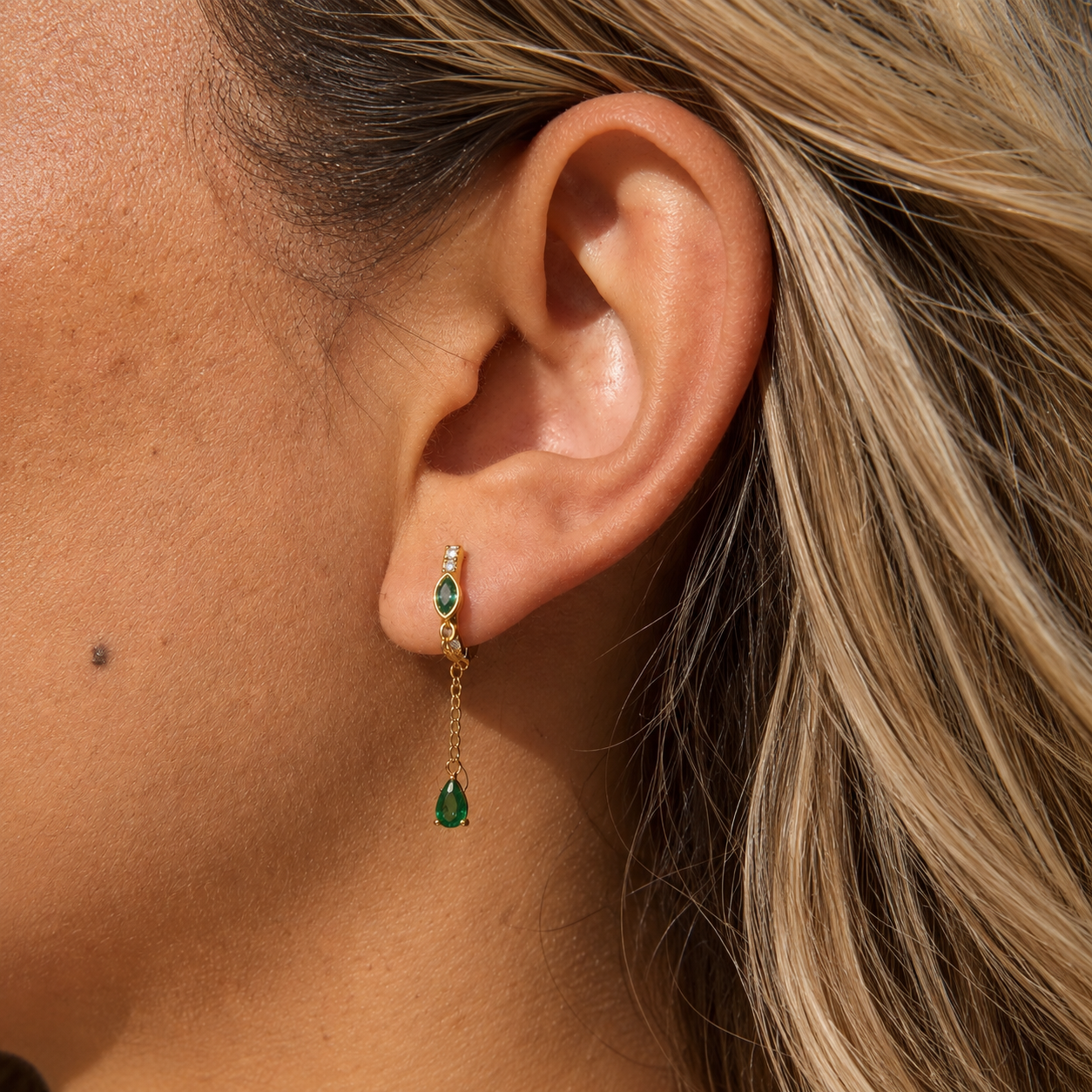Model wearing Sallie waterproof gold tassel huggie earrings with emerald green stones.