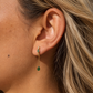 Model wearing Sallie waterproof gold tassel huggie earrings with emerald green stones.