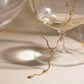 Saya gold Y necklace with crystal accents draped over a glass coupe on a neutral background