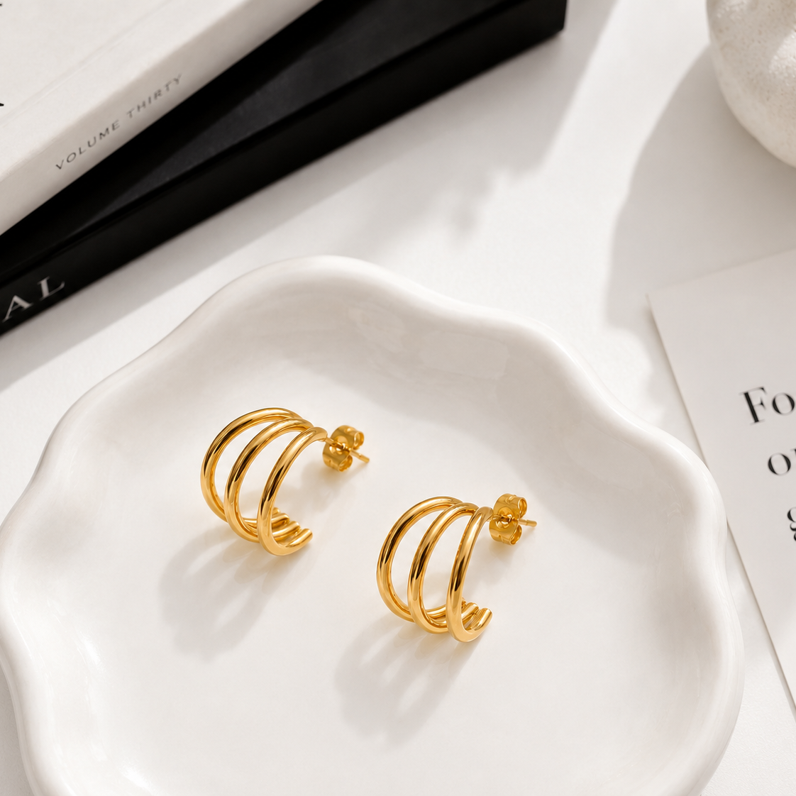 Shanti waterproof triple gold hoop earrings styled in a minimal luxury flat lay, featuring three sculptural gold bands.