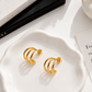 Shanti waterproof triple gold hoop earrings styled in a minimal luxury flat lay, featuring three sculptural gold bands.