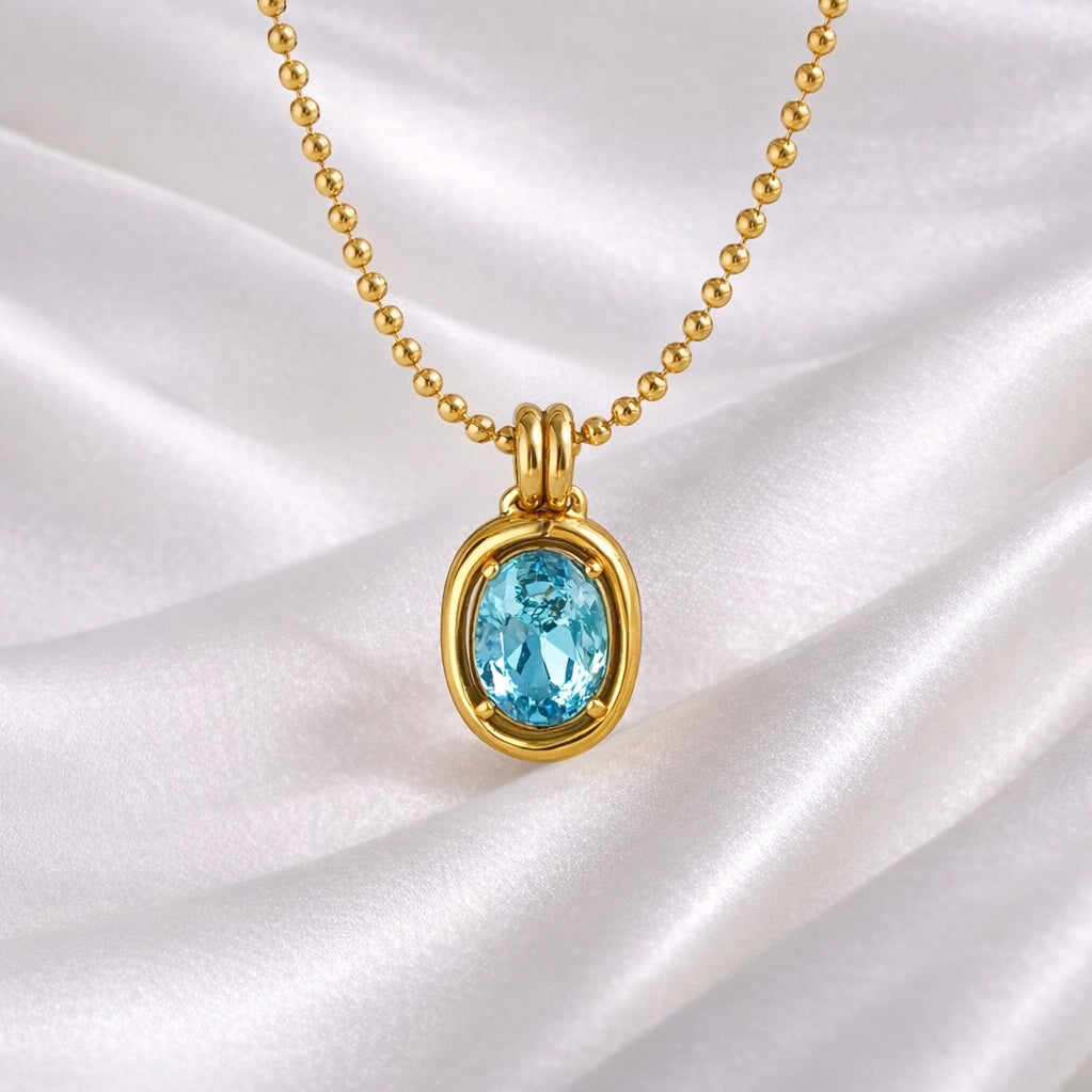 Close-up of Skye light aqua oval gemstone pendant necklace in 18K gold plated stainless steel on white silk background