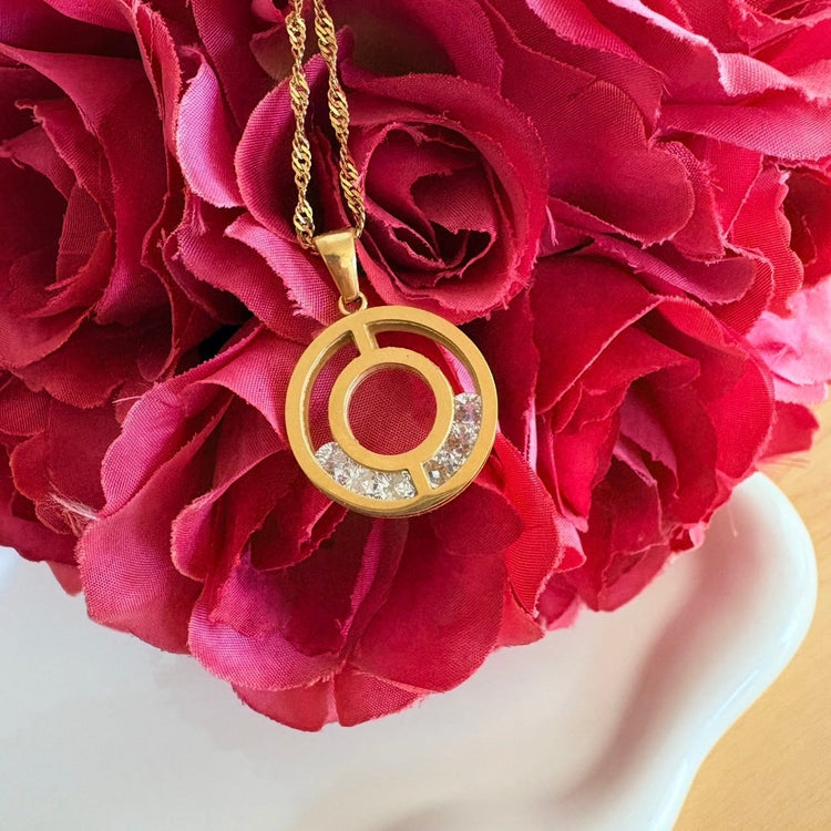 Stephanie gold circle pendant necklace with cubic zirconia detail styled on red flowers