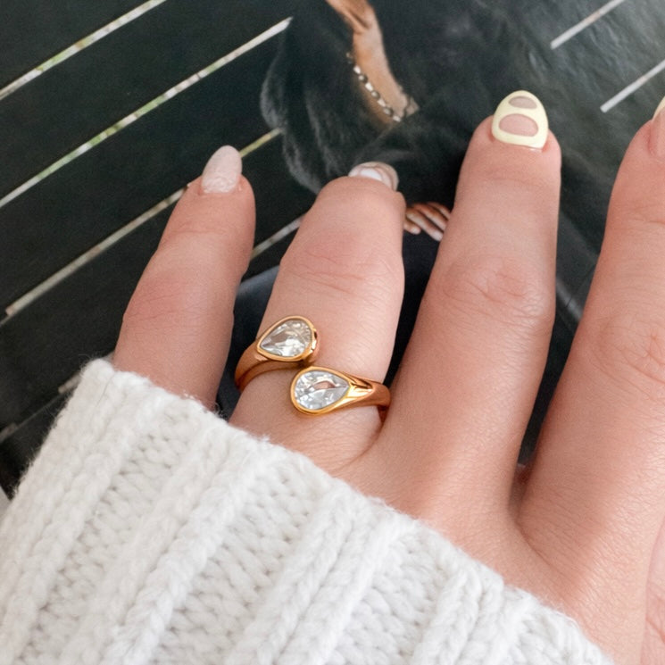 Hand wearing the Suzana Ring, a gold open ring with two sparkling pear-cut crystals
Image Title: Suzana Ring Styled on Hand