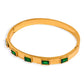Gold Abby bangle bracelet with five emerald green baguette stones on a white background.