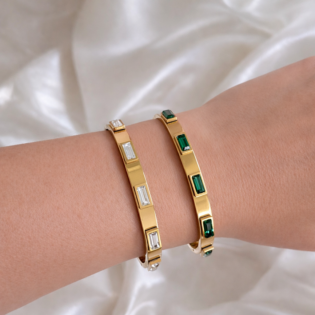 Two Abby bangle bracelets with clear and emerald green baguette stones worn stacked on a wrist