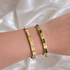 Two Abby bangle bracelets with clear and emerald green baguette stones worn stacked on a wrist